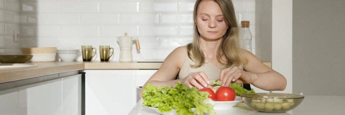 Woman sitting at table preparing fresh vegetables in a modern kitchen, highlighting healthy living and independence.